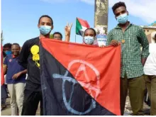 Three Sudanese Anarchists hold a black and red flag
