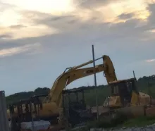 four construction vehicles with broken windows, one of them is nothing but charred remains, and next to it is another charred vehicle 