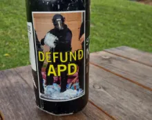 A glass bottle with a sticker of a cop in riot gear holding a pack of leaking water bottles? A glass bottle with a sticker of a cop in riot gear holding a pack of leaking water bottles?